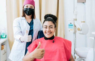 Obraz premium Female dentist with satisfied patient smiling at camera and giving thumb up, Female dentist with patient smiling and giving thumb up. Portrait of female dentist with patient smiling in office