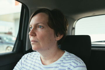 Woman sitting at the back seat of the passenger car and looking out the vehicle window