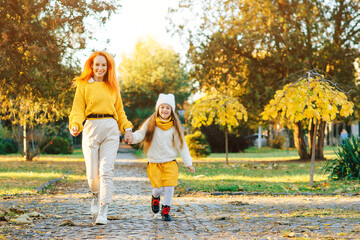 Fototapeta premium Happy mother and daughter walking in the park. Family enjoying the beautiful autumn nature.