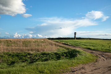 A water tower in the distance, fields, a winding road, blue skies, white clouds.