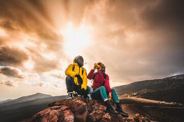 Multiethnic couple of young people hikers relaxing on the peak of the mountain watching the...