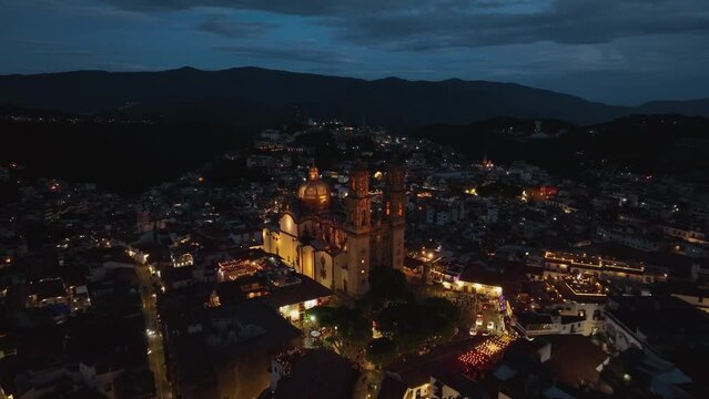 Aerial view towards the illuminated Church of Santa Prisca de Taxco, night in Mexico - approaching, drone shot