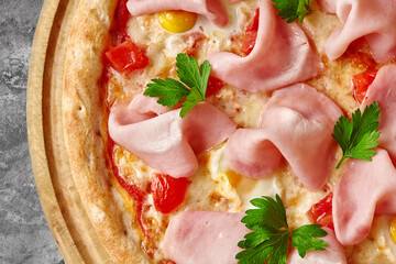 Closeup of pizza with mozzarella, ham slices, quail eggs, tomatoes and greens on wooden serving board