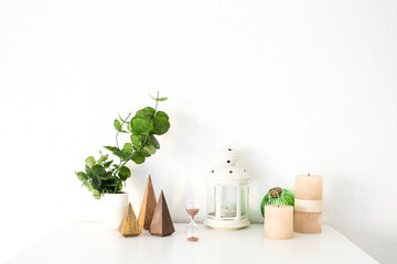 White lantern candle holder, wood Christmas trees, green plant, ball, candles and hourglass on white table. Christmas interior decoration