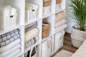 Fototapeta na wymiar Neatly folded linen cupboard shelves storage at eco friendly straw basket placed closet organizer
