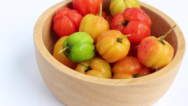 Barbados cherry, Malpighia emarginata, red acerola cherry in wooden bowl. Selective focus. Rotating on turn table. 