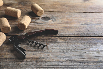Opener with corkscrew and corks on wooden table, space for text