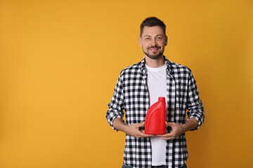 Man holding red container of motor oil on orange background. Space for text