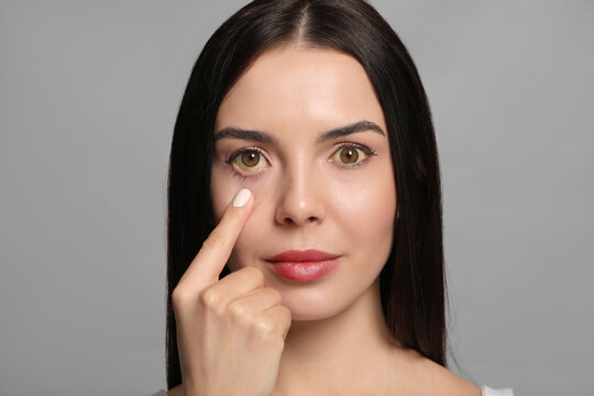 Woman checking her health condition on grey background. Yellow eyes as symptom of problems with liver