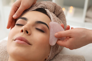 Young woman receiving facial massage with gua sha tool in beauty salon, closeup