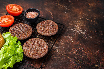 Grilled hamburger patties with tomatoes and seasonings on kitchen table. Dark background. Top view. Copy space