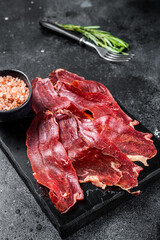 Turkish sliced pastrami (kayseri pastirma), dried beef meat with spices on marble board. Black background. Top view
