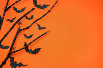 Flat lay composition with black branches, paper bats and spiders on orange background, space for text. Halloween celebration