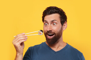 Emotional man holding sushi roll with chopsticks on orange background © New Africa
