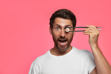 Funny man hiding his eye with tasty sushi roll on pink background. Space for text © New Africa