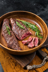 Fried sirloin flap or flank beef steak with herbs in a wooden plate. Black background. Top view