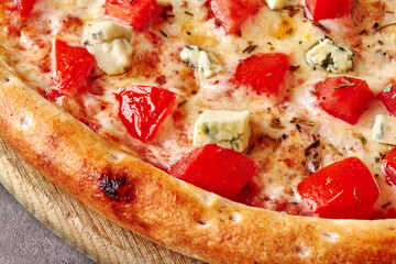 Closeup of pizza with mozzarella, tomatoes, blue cheese and dried basil on wooden board