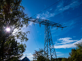 Strommast mit sechs Leitungen vor blauem Himmel und seitlich reinragenden Baum