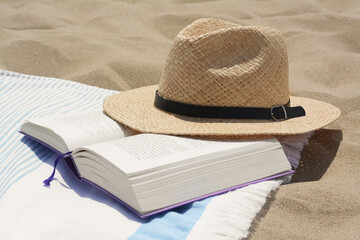 Beach towel with open book and straw hat on sand