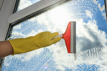 Woman cleaning glass with squeegee indoors, closeup