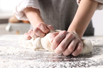 Woman kneading dough at table in kitchen, closeup