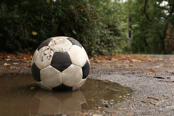 Dirty soccer ball in muddy puddle, space for text