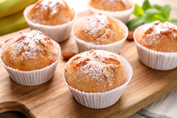 Tasty muffins powdered with sugar on wooden board, closeup