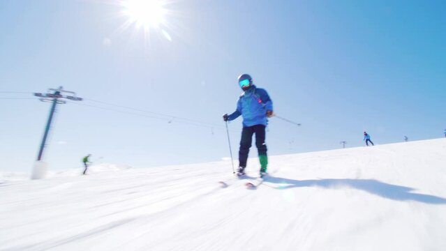 Skier skiing on slopes in winter ski center. Sun rays and lens flare visible.