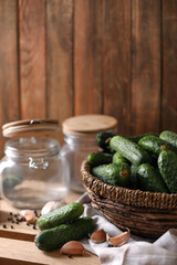 Fresh cucumbers and other ingredients near empty jars prepared for canning on wooden table