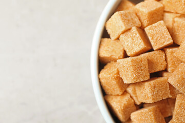 Brown sugar cubes in bowl on light grey table, top view. Space for text