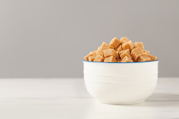 Brown sugar cubes in bowl on white table, space for text