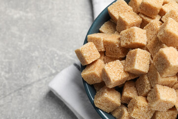 Brown sugar cubes in bowl on light grey table, top view. Space for text