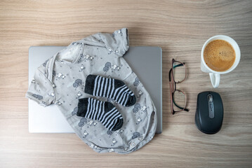 Baby socks, baby onesie, coffee, glasses laptop on wooden table indoors symbolising maternity or...