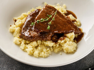 Close up view of sliced roasted beef with mashed potato on plate over grey background