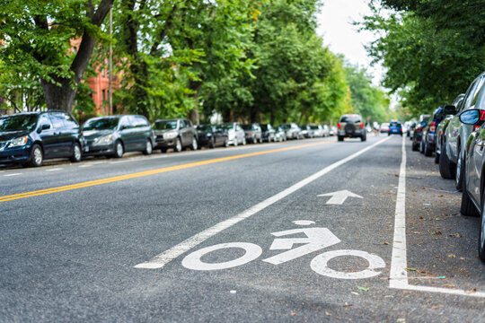 carril bici con señal pintada en el asfalto de la calle y con coches aparcados y coche de fondo