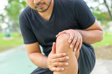 A young male in sports outfits black injured his knee during exercise in the park. Low section of sports man suffering from joint pain while sitting on track during. Accident from exercise concept.