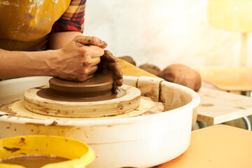 A Potter works with red clay on a Potter's wheel in the workshop..Women's hands create a pot. Girl sculpts in clay pot closeup. Modeling clay close-up. 