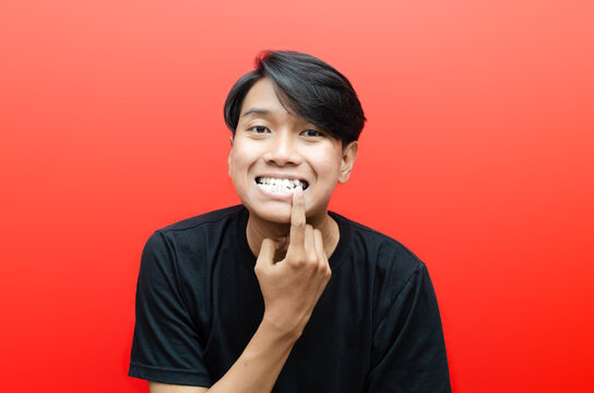 young asian man showing his crooked teeth or gigi gingsul isolated over red background. dracula teeth and bucktooth concept. overlapping teeth of man