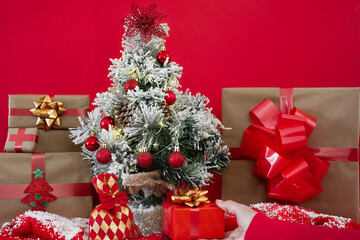 Small decorated Christmas tree and female hand offering a present. Copy space on red background