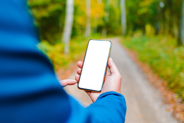 Blank space mockup.Hiker man standing on a trail autumn forest and showing of smartphone white screen.Technology in nature concept.Selective focus.