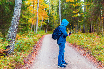 Man hiker lost in a autumn forest and search a mobile network on a hone.Tourist looking for a cellular connection on a hike.Full lenght hiker stand on the road.Travel Technology concept.