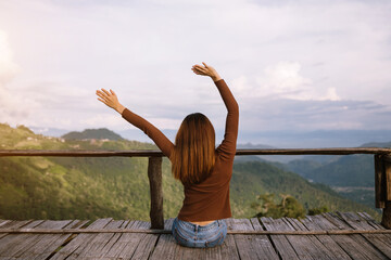 Rear view image of a female traveler sitting and looking at a beautiful mountain,sky field and nature