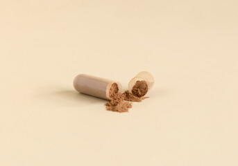 Opened Medical capsule to show brown powder on light beige close up. Dietary supplements