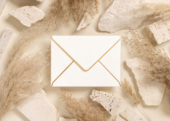 Envelope near beige travertine stones and dried pampas grass top view, greeting mockup