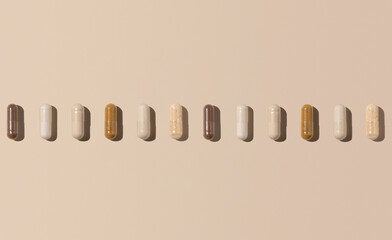 Mix of medical capsules in a line on light beige top view, hard shadows. Dietary supplements
