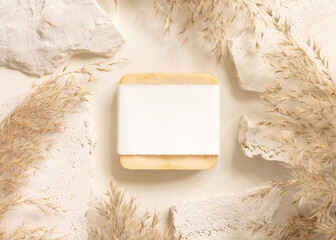 Soap bar with blank label near beige stones and dried pampas grass top view, mockup