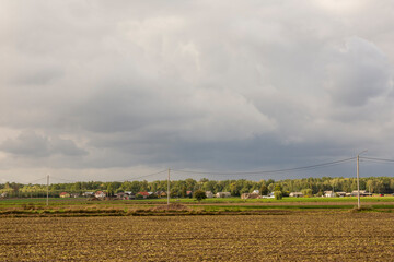 Fototapeta na wymiar Dark clouds over the plowed field and the village in the background. Autumn.