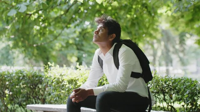 Sad young man sitting on bench at city park observe surroundings, static