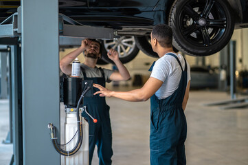 Fototapeta Two professional mechanics performing visual inspection of the vehicle underbody obraz