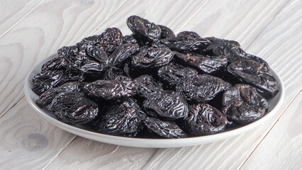 Prunes, vegetarian food. In a white plate on a white wooden background.